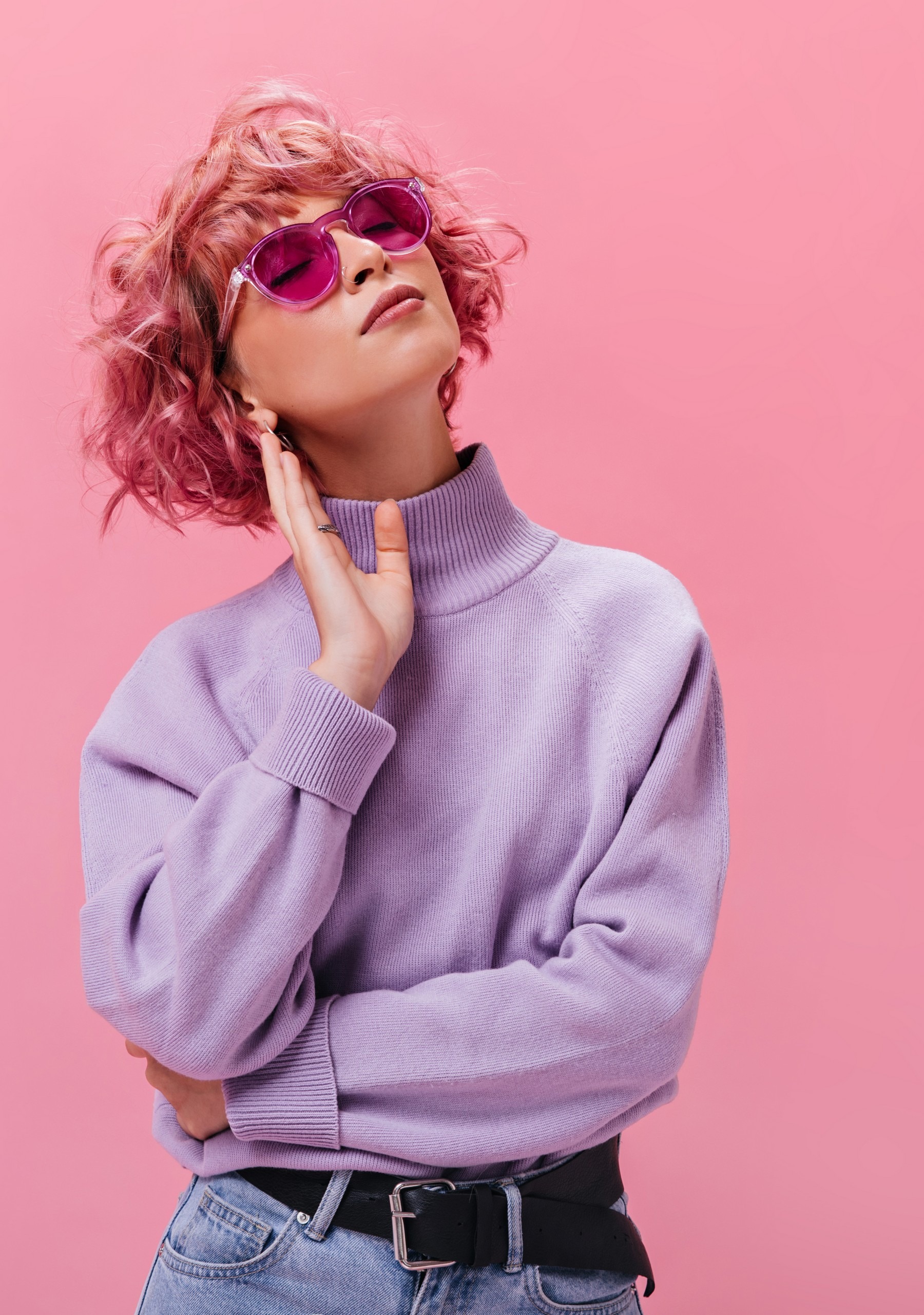 Attractive curly woman in purple cashmere sweater and fuchsia sunglasses poses on isolated background. Portrait of short-haired girl on pink backdrop .